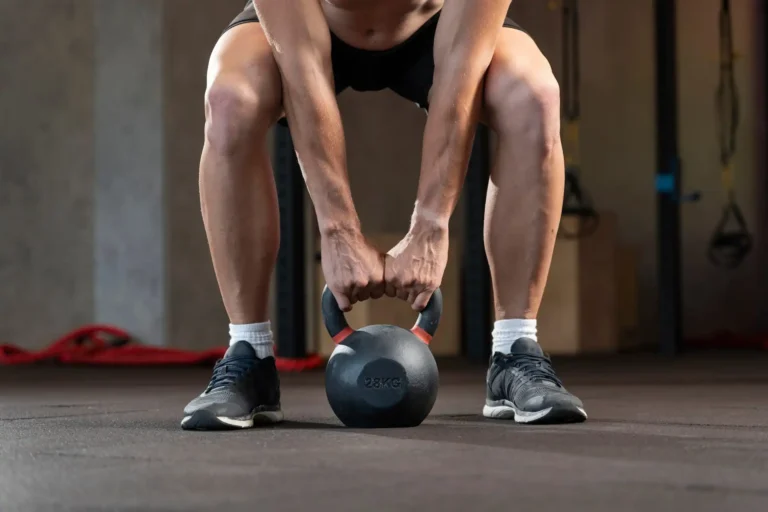 Primo piano sulle gambe di un uomo in squat che sta per sollevare un peso kettlebell
