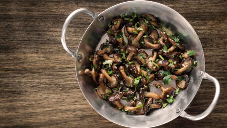 Pentola in acciaio con funghi cotti al prezzemolo su un tavolo di legno