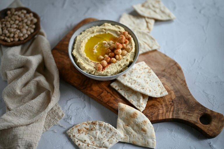 Una ciotola di hummus di ceci su un tagliere con alcune fette di piadina